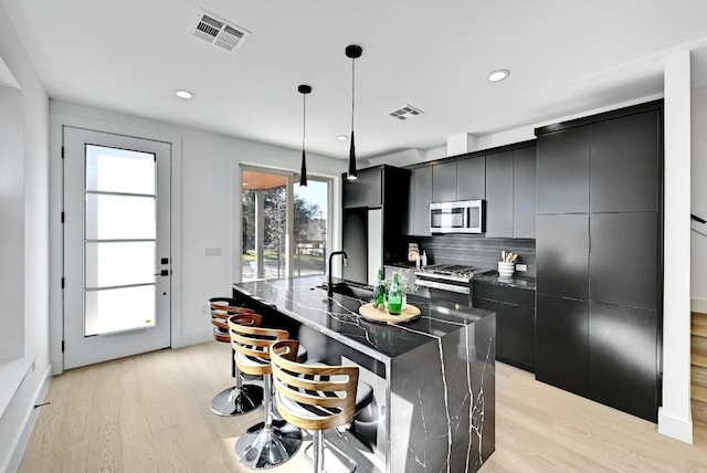 kitchen with appliances with stainless steel finishes, visible vents, light wood-style flooring, and dark cabinetry