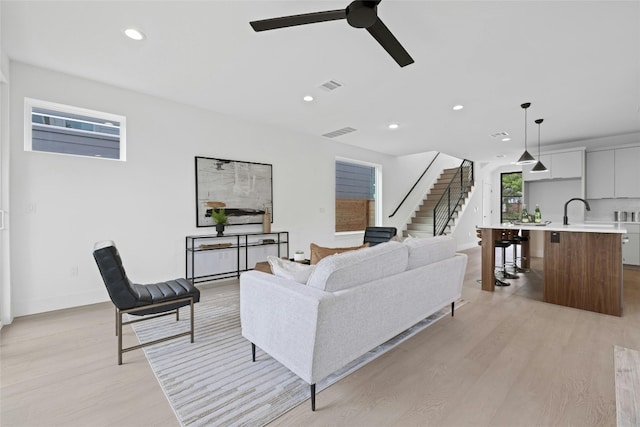 living room with light wood-type flooring, ceiling fan, and sink