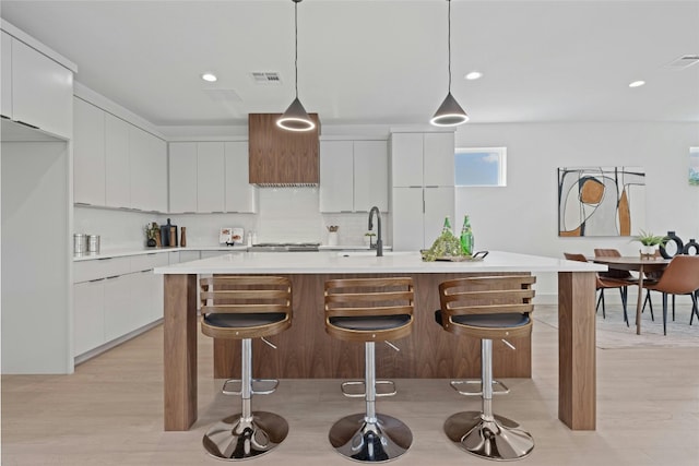 kitchen featuring white cabinets, pendant lighting, and an island with sink