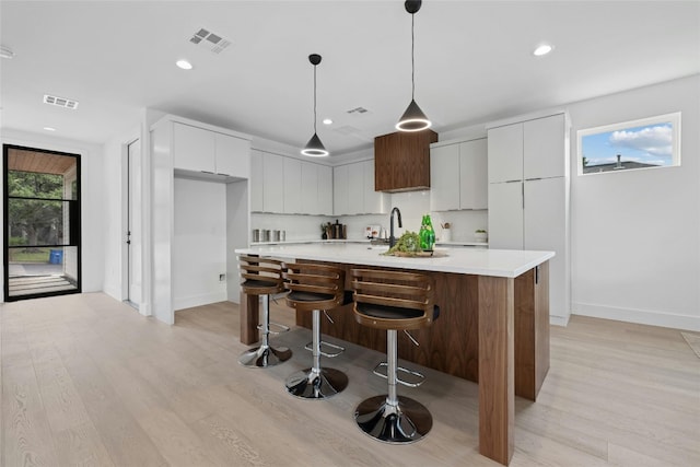 kitchen featuring white cabinetry, light hardwood / wood-style flooring, a kitchen island with sink, and hanging light fixtures