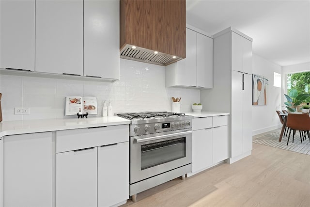 kitchen with custom exhaust hood, backsplash, white cabinetry, stainless steel gas range, and light hardwood / wood-style floors