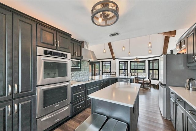 kitchen with tasteful backsplash, range hood, appliances with stainless steel finishes, decorative light fixtures, and kitchen peninsula