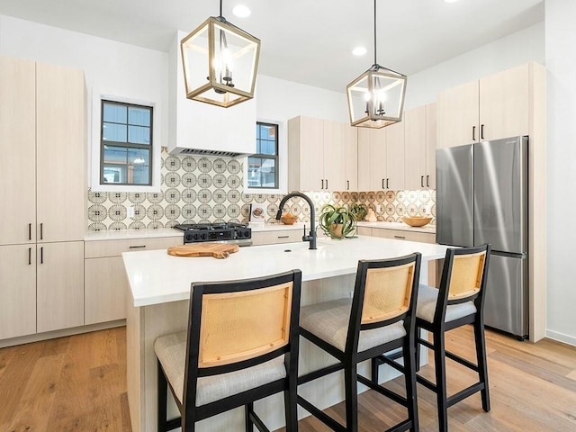 kitchen featuring stainless steel refrigerator, an inviting chandelier, an island with sink, and pendant lighting