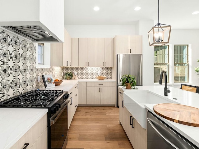 kitchen with premium range hood, decorative light fixtures, sink, light hardwood / wood-style floors, and stainless steel appliances