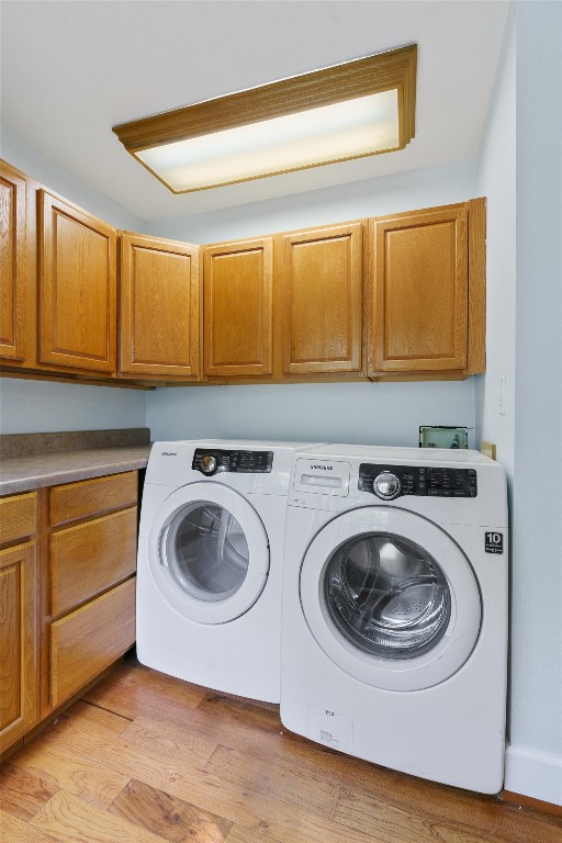 clothes washing area featuring washer hookup, light hardwood / wood-style flooring, washing machine and dryer, and cabinets