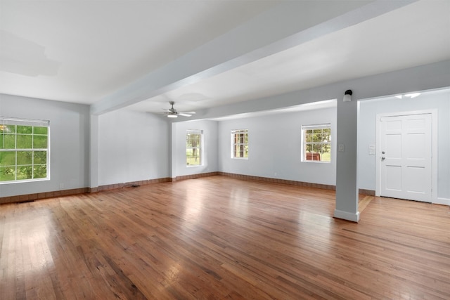 empty room with beamed ceiling, light hardwood / wood-style floors, and ceiling fan