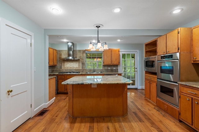 kitchen featuring a center island, appliances with stainless steel finishes, wall chimney range hood, and light hardwood / wood-style floors