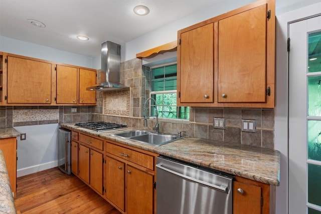 kitchen featuring tasteful backsplash, appliances with stainless steel finishes, wall chimney range hood, and light hardwood / wood-style flooring