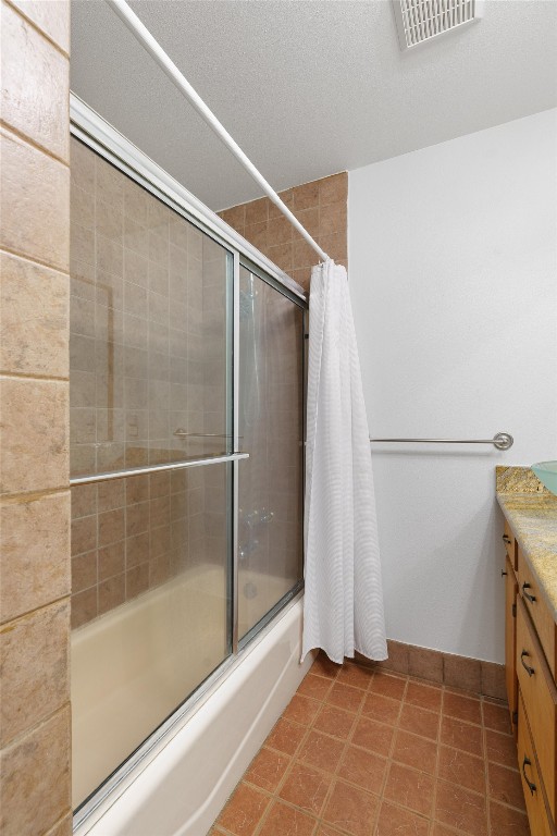 bathroom featuring a textured ceiling, vanity, tile floors, and bath / shower combo with glass door