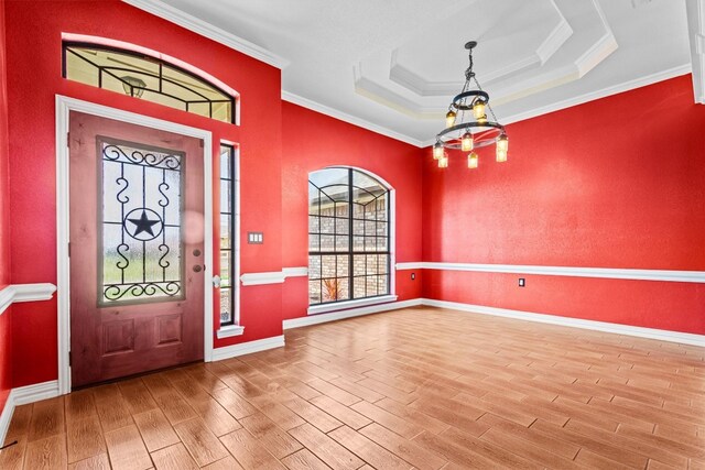 entryway featuring ornamental molding, a notable chandelier, a raised ceiling, and light wood-type flooring