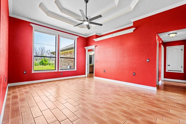 empty room with crown molding, ceiling fan, a raised ceiling, and light wood-type flooring