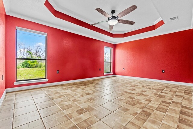 empty room with light tile floors, crown molding, ceiling fan, and a raised ceiling