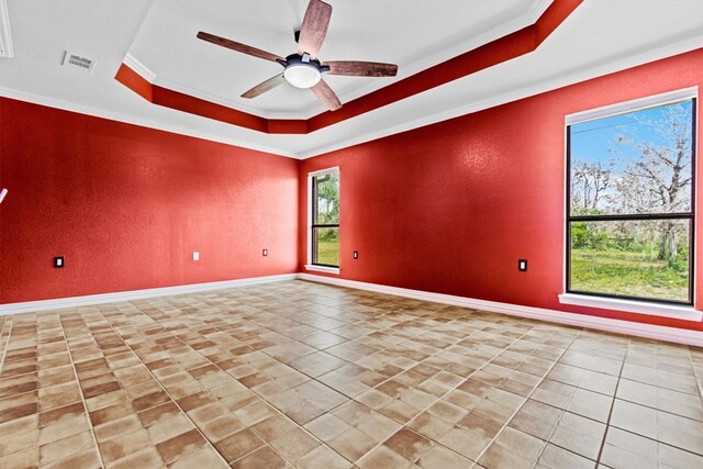 tiled empty room with crown molding, ceiling fan, and a tray ceiling