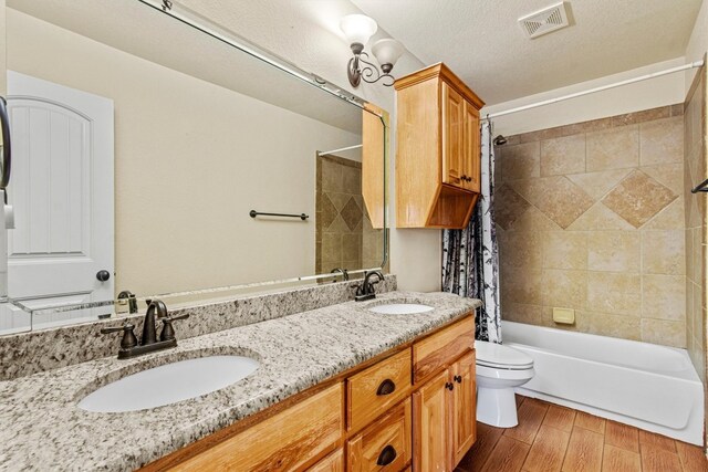 full bathroom with large vanity, toilet, tiled shower / bath combo, a textured ceiling, and dual sinks