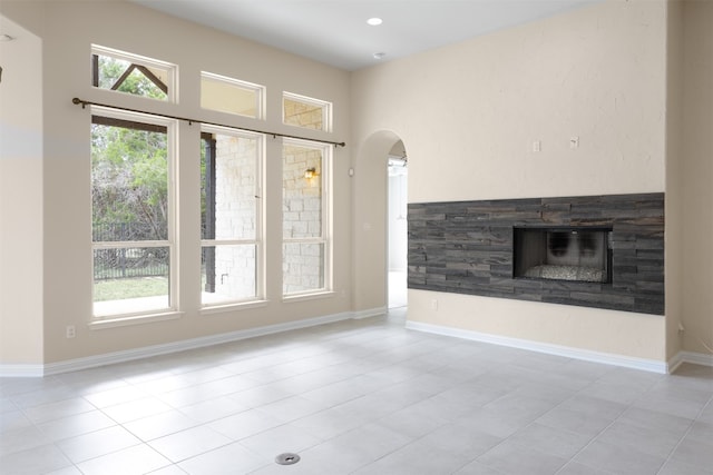 empty room featuring a stone fireplace, light tile floors, and a wealth of natural light