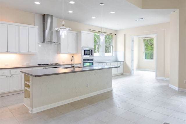 kitchen featuring wall chimney exhaust hood, pendant lighting, white cabinetry, stainless steel appliances, and sink