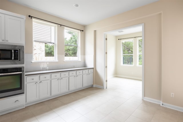 kitchen featuring backsplash, appliances with stainless steel finishes, white cabinetry, and light tile floors