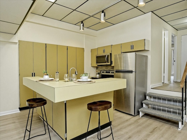 kitchen featuring light hardwood / wood-style flooring, tasteful backsplash, rail lighting, a breakfast bar area, and appliances with stainless steel finishes