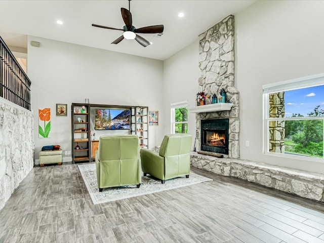 living room with light hardwood / wood-style floors, ceiling fan, a towering ceiling, and a fireplace