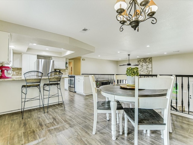 dining space featuring ceiling fan with notable chandelier, a tray ceiling, and light wood-type flooring