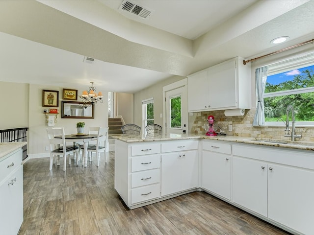 kitchen with light stone counters, white cabinets, sink, light hardwood / wood-style flooring, and an inviting chandelier