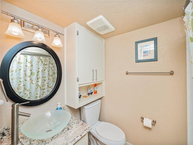 bathroom featuring toilet, a textured ceiling, vanity, and visible vents