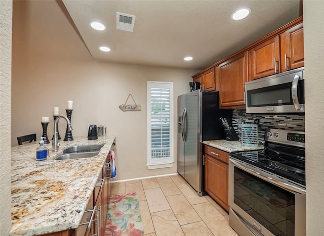 kitchen featuring appliances with stainless steel finishes, light tile floors, sink, tasteful backsplash, and light stone countertops