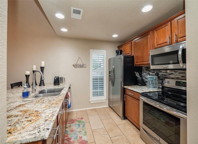 kitchen with tasteful backsplash, visible vents, appliances with stainless steel finishes, light stone countertops, and a sink