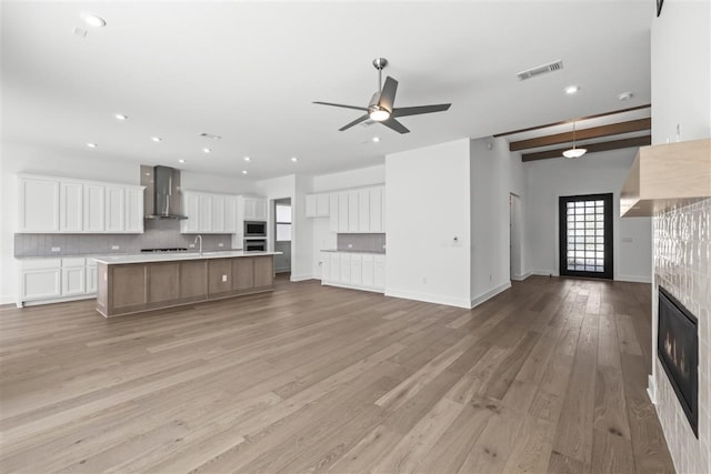 unfurnished living room featuring sink, ceiling fan, light wood-type flooring, a fireplace, and beam ceiling