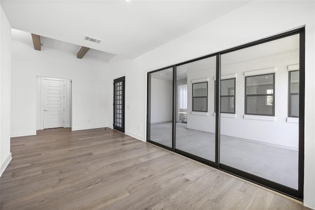 unfurnished bedroom with hardwood / wood-style floors, beam ceiling, and a closet