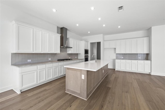 kitchen with white cabinets, wall chimney exhaust hood, a spacious island, and hardwood / wood-style floors