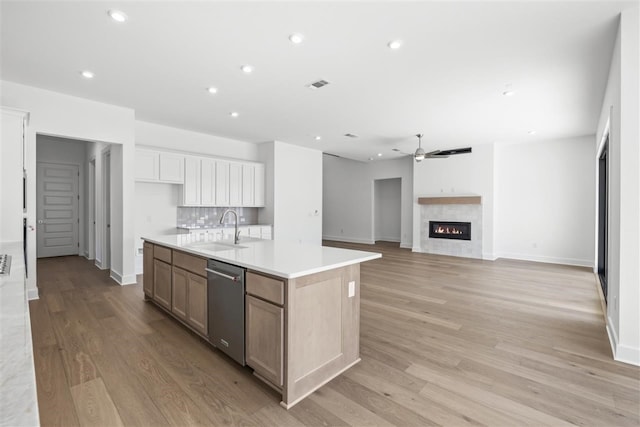 kitchen with white cabinetry, dishwasher, sink, light hardwood / wood-style floors, and a center island with sink