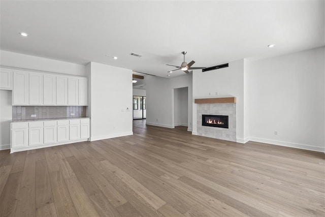 unfurnished living room featuring ceiling fan, light wood-type flooring, and a tile fireplace