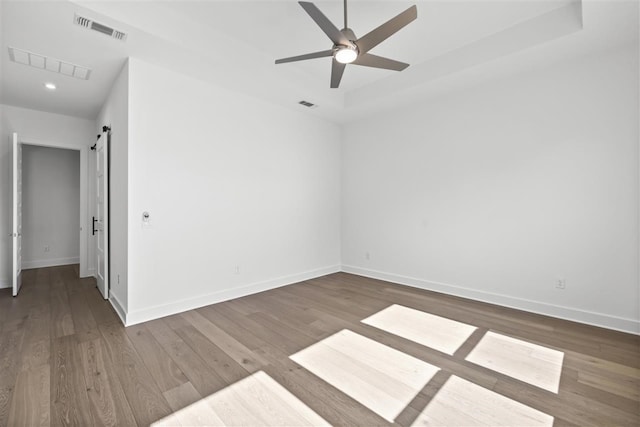 empty room with a barn door, ceiling fan, and dark hardwood / wood-style flooring