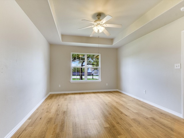 unfurnished room featuring ceiling fan, a raised ceiling, and light wood-type flooring