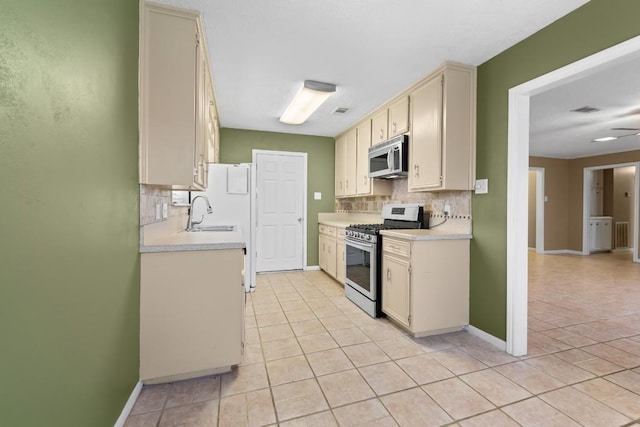 kitchen featuring stainless steel appliances, light tile patterned floors, decorative backsplash, and cream cabinetry