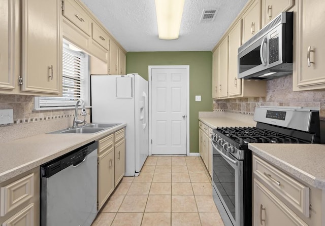 kitchen with sink, a textured ceiling, light tile patterned floors, stainless steel appliances, and cream cabinetry