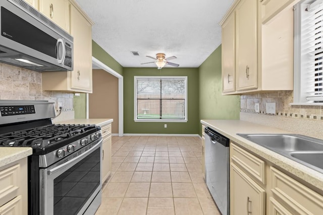 kitchen with stainless steel appliances, light tile patterned floors, ceiling fan, and cream cabinetry