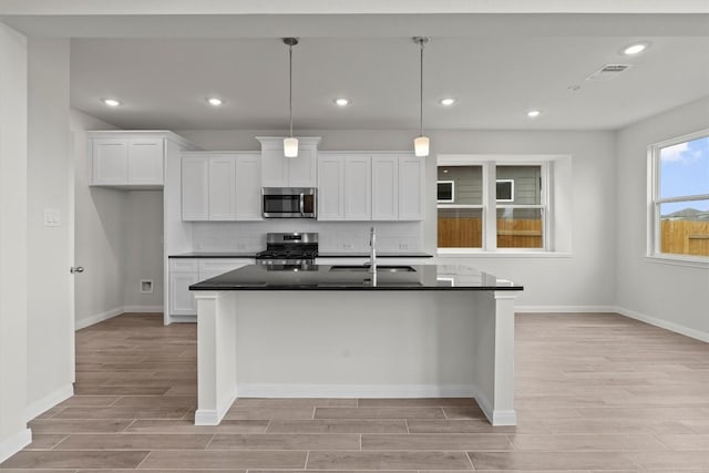 kitchen with decorative backsplash, stainless steel appliances, pendant lighting, a center island with sink, and white cabinets