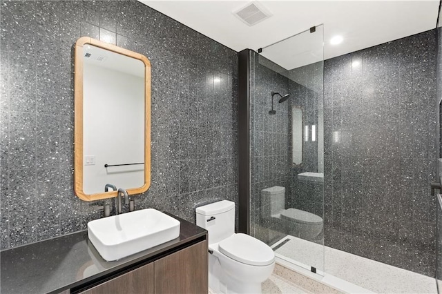 bathroom with visible vents, toilet, walk in shower, vanity, and tile walls