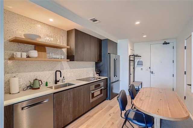 kitchen featuring stainless steel appliances, light countertops, backsplash, a sink, and light wood-type flooring