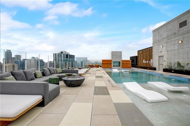 view of pool featuring a view of city, a patio area, and an outdoor living space with a fire pit