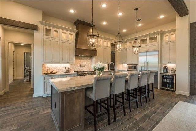 kitchen with beverage cooler, dark wood-type flooring, custom range hood, a center island with sink, and tasteful backsplash