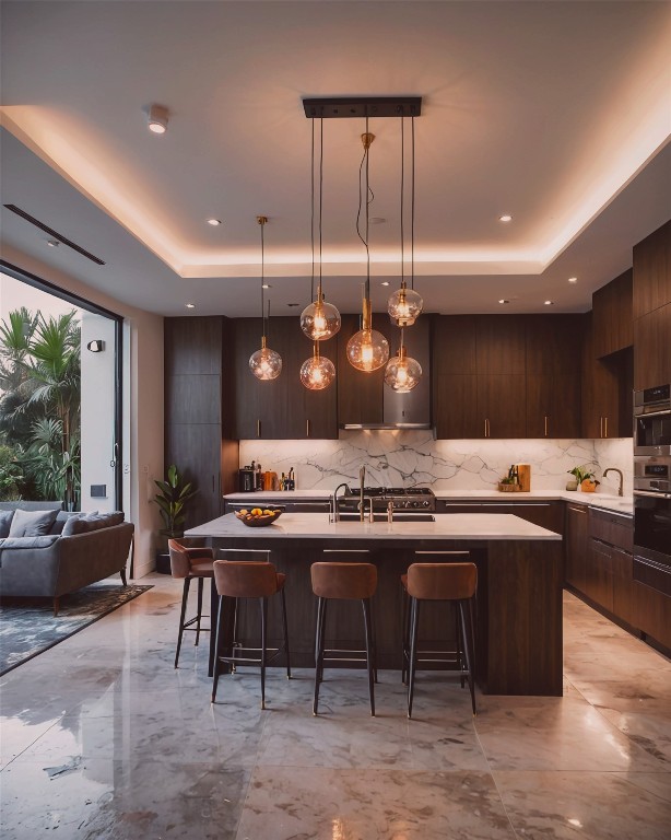 kitchen with hanging light fixtures, a kitchen breakfast bar, a raised ceiling, and an island with sink