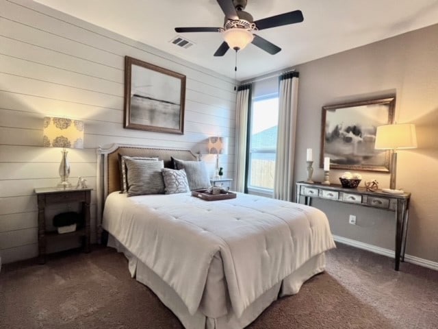 bedroom with ceiling fan, dark carpet, and wooden walls