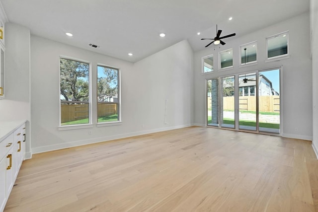 unfurnished living room with light hardwood / wood-style flooring, a wealth of natural light, a high ceiling, and ceiling fan