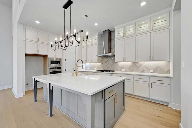 kitchen with wall chimney exhaust hood, white cabinetry, and a kitchen island with sink