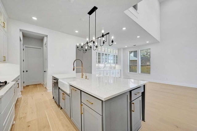 kitchen featuring an island with sink, light hardwood / wood-style flooring, stainless steel dishwasher, sink, and gray cabinets