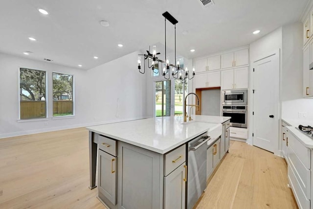 kitchen featuring an island with sink, light hardwood / wood-style flooring, stainless steel appliances, a notable chandelier, and gray cabinets