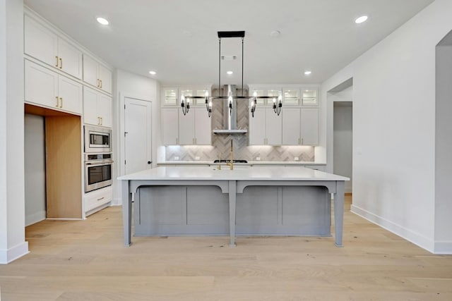 kitchen with an island with sink, light hardwood / wood-style flooring, stainless steel appliances, range hood, and white cabinets